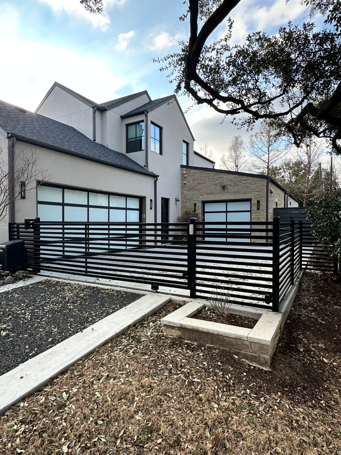 Matte black sliding driveway gate in a matching horizontal slat design, rolling on a floor track beside an operator box, with matching fence panels enclosing the courtyard of a modern home.