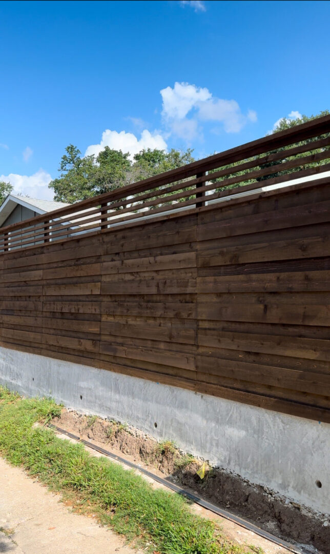 Dark stained horizontal cedar privacy fence set on a low concrete retaining wall, topped with a slatted screen and a flat cap rail along a yard edge.